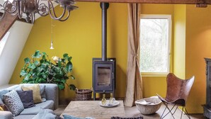 A cozy living room with a sofa, a chair, a table, a large plant, and a wood-burning stove. - 3 bedroom pet friendly home in Leende (Leende)