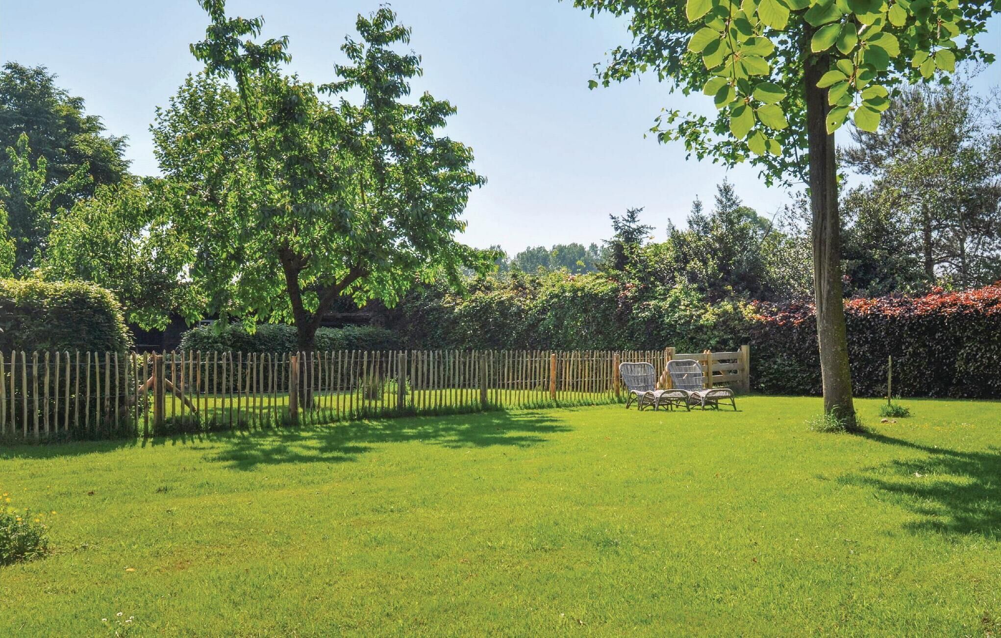 Ein gepflegter Garten mit Holzzaun, Rasenfläche und einer Sitzgelegenheit mit Stühlen.