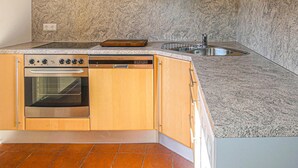 A kitchen with a built-in oven, dishwasher, granite countertop, and stainless steel sink.