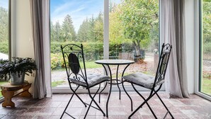 A patio with a table and chairs, a potted plant, and a view of a garden through a glass door.