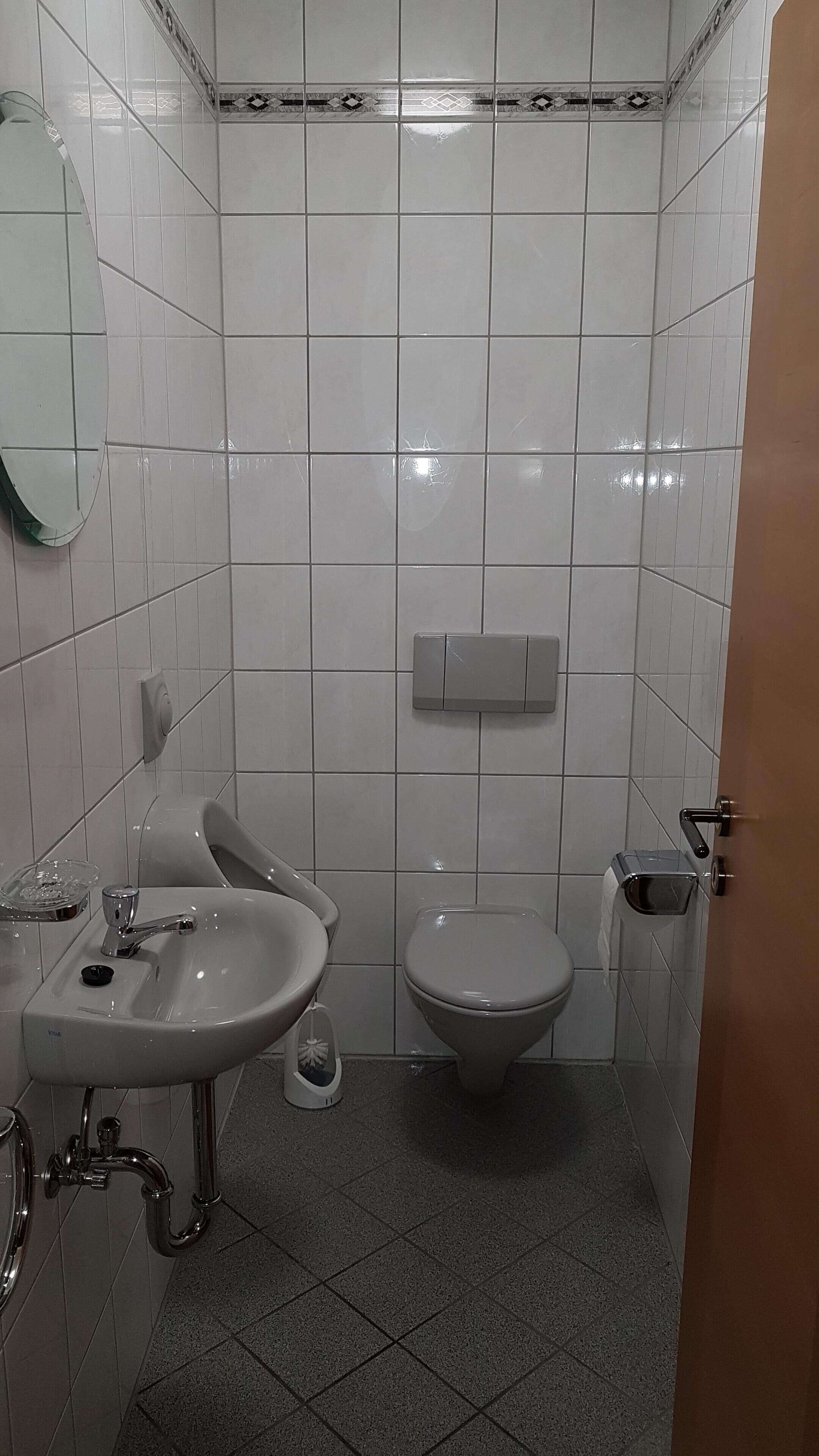 A small, clean bathroom with white tiles, a sink, a toilet, and a mirror.