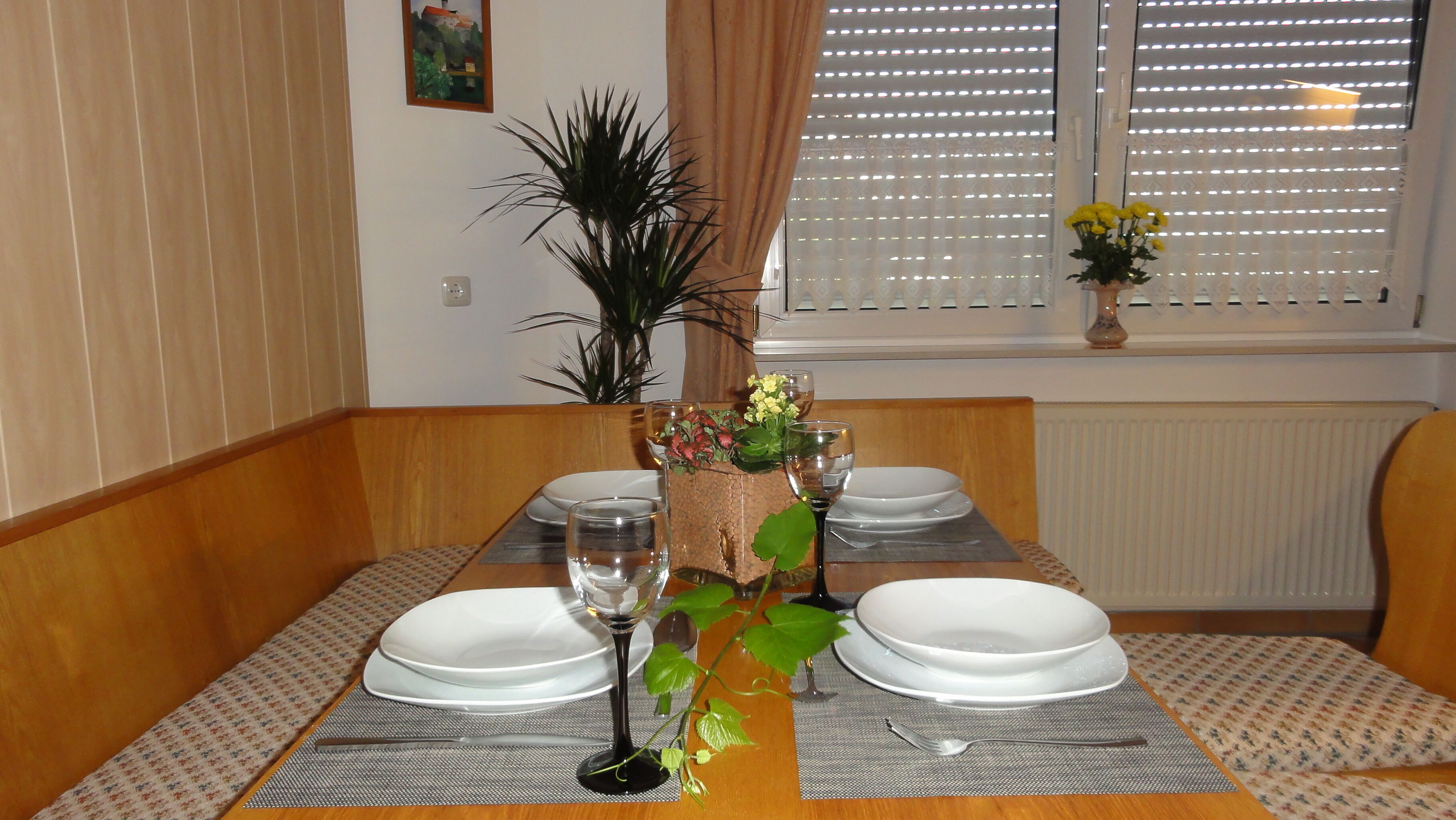 A dining table set with white plates, wine glasses, and a centerpiece of flowers and greenery.