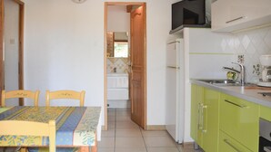 A kitchen with green cabinets, a white refrigerator, and a sink. There is a dining table with chairs in the foreground. - 2 bedroom beautiful home in Gordes (Gordes)