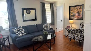 A living room with a blue sofa, patterned pillows, a coffee table, a side table with a lamp, and a framed picture on the wall.
