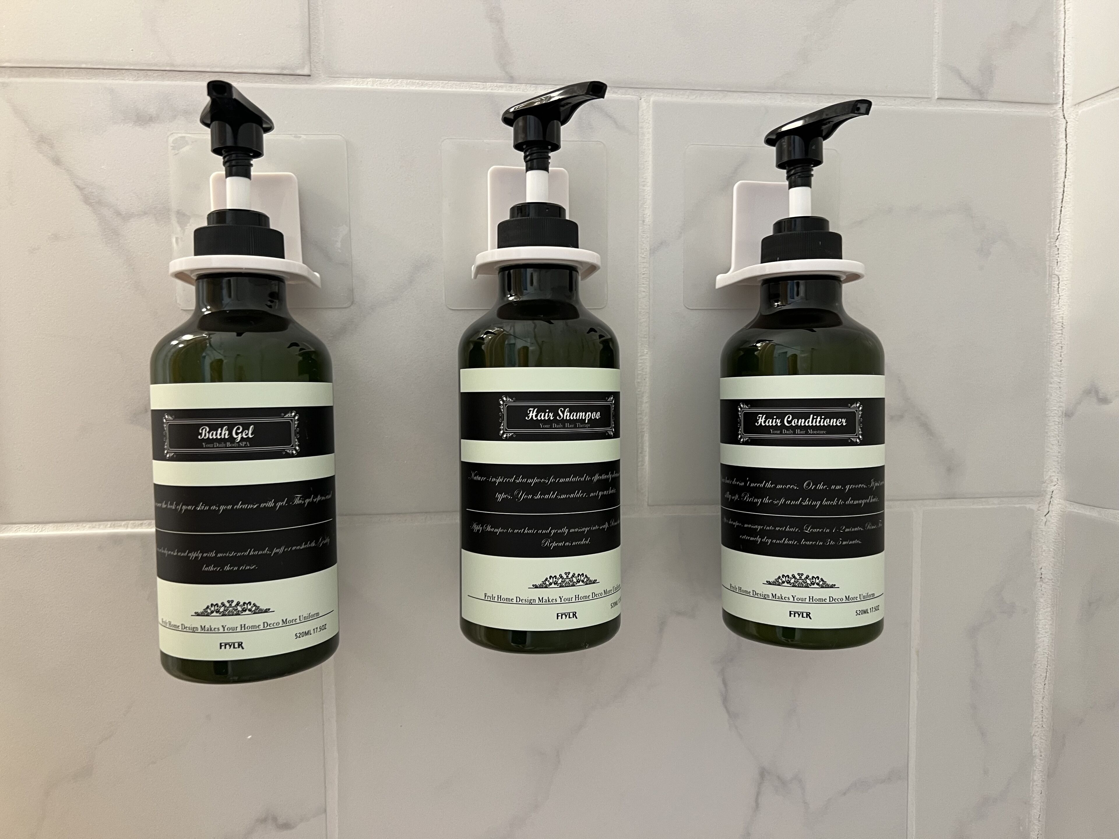 Three bottles of bath products on a tiled wall.