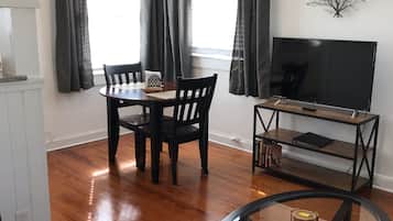 A living room with a dining table, chairs, a TV on a stand, and a glass-top coffee table.