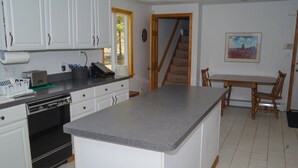 A kitchen with white cabinets, a granite countertop, a built-in oven, and a dining area with wooden chairs and a table. - Wachusett Mountain Getaway, Lake Adjacent Home! Near 1761 Old Mill and Trails! (Westminster)