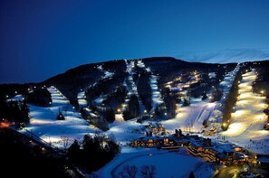 Une station de ski enneigée, illuminée la nuit, avec des pistes et des bâtiments éclairés.