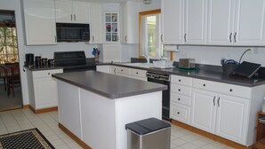 A modern kitchen with white cabinetry, a central island, stainless steel appliances, and a tiled floor. - Wachusett Mountain Getaway, Lake Adjacent Home! Near 1761 Old Mill and Trails! (Westminster)
