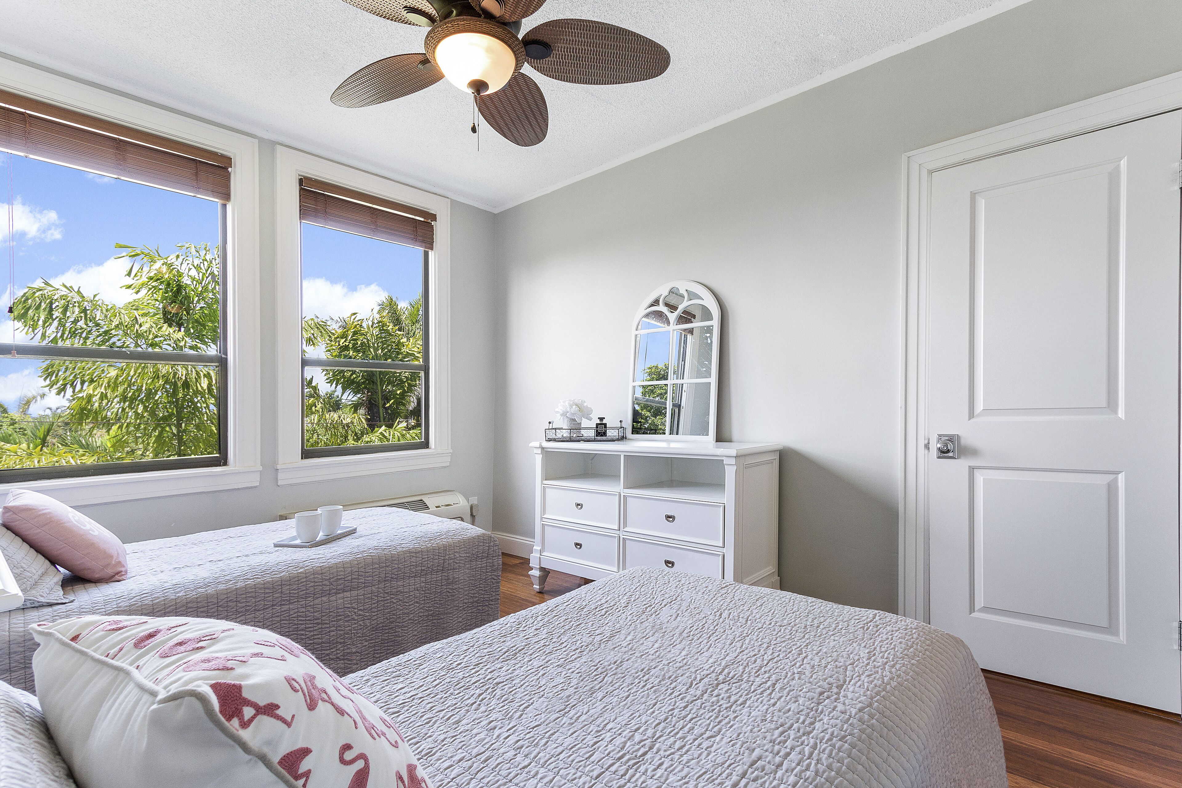 Quarto com duas camas, cômoda, espelho e ventilador de teto.