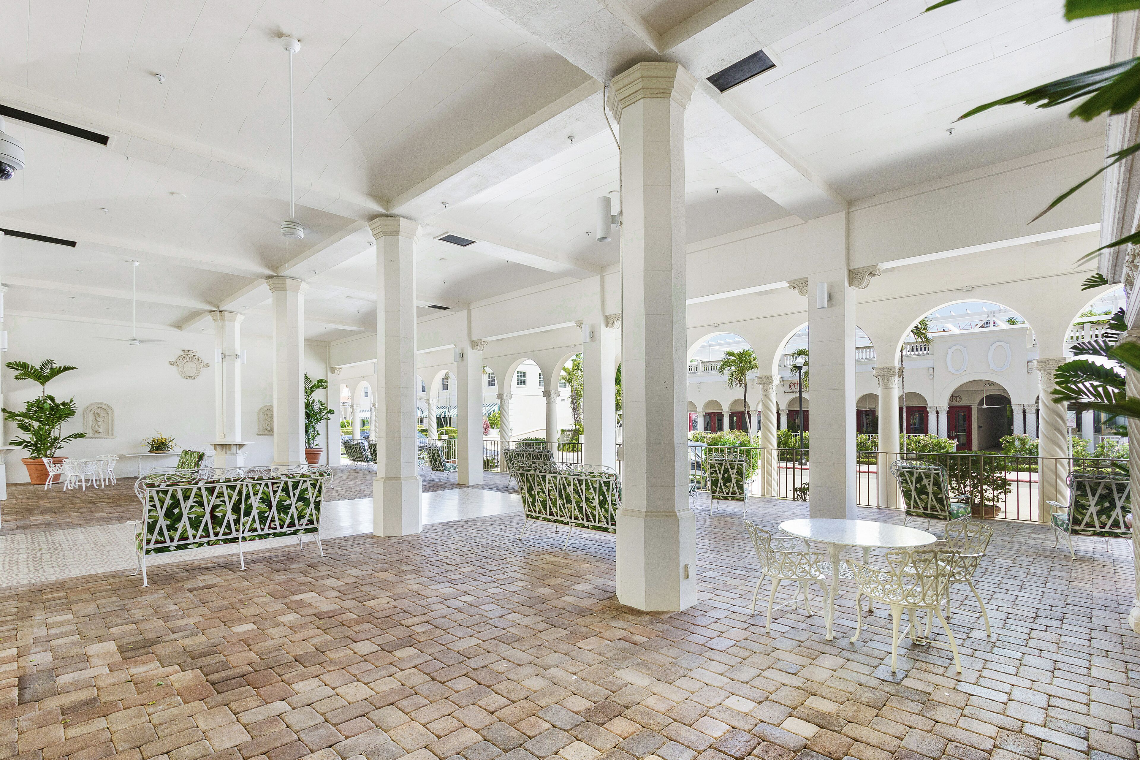 A spacious courtyard with white columns, brick flooring, and outdoor seating areas.