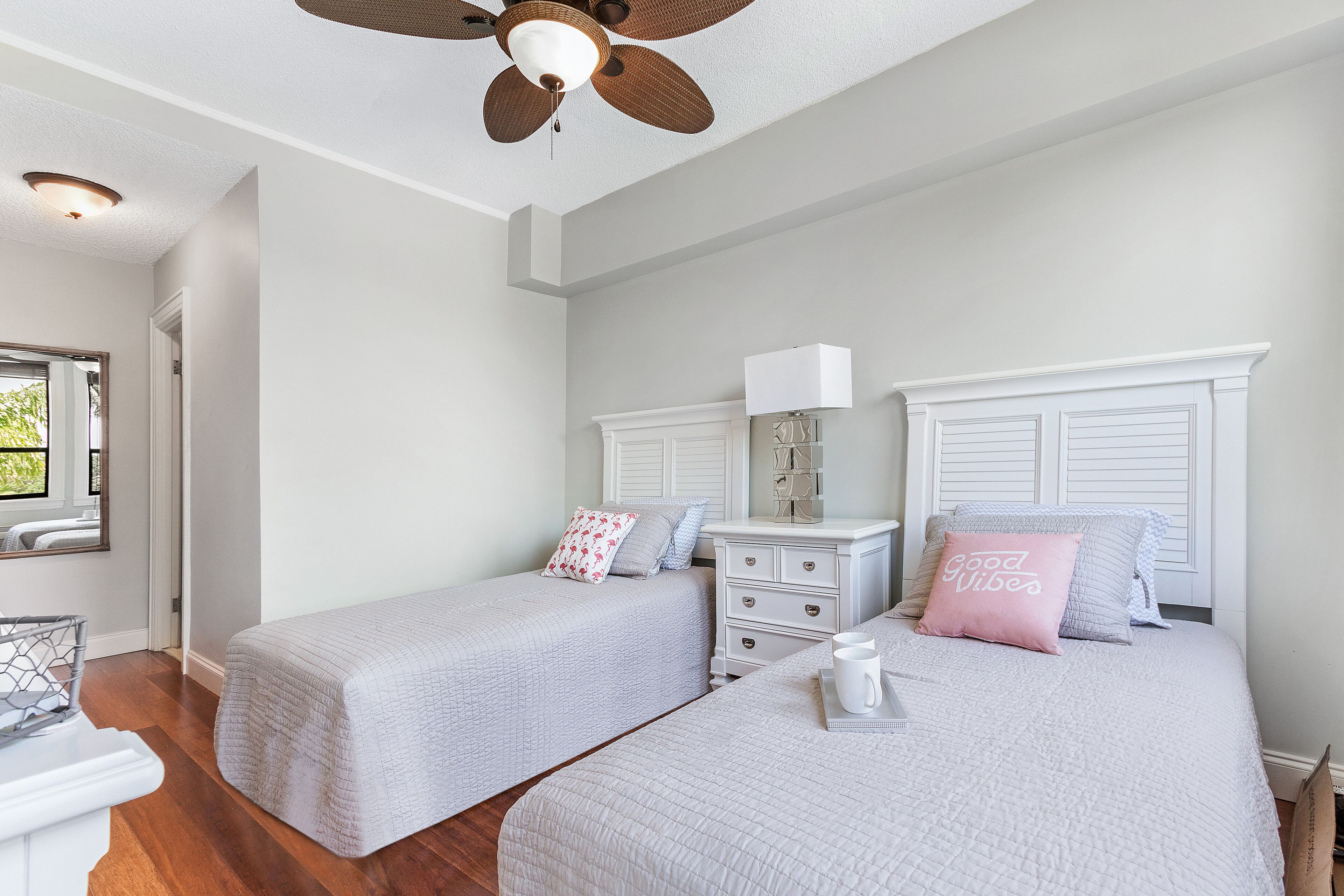 A bedroom with two beds, a nightstand, a dresser, a ceiling fan, and a window with blinds.