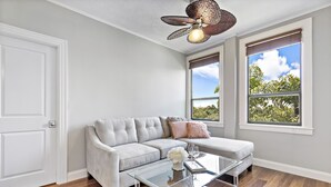 A modern living room with a grey sectional sofa, a glass coffee table, and a ceiling fan. - Luxury 2 bedroom condo on Palm Beach Island! (Palm Beach)