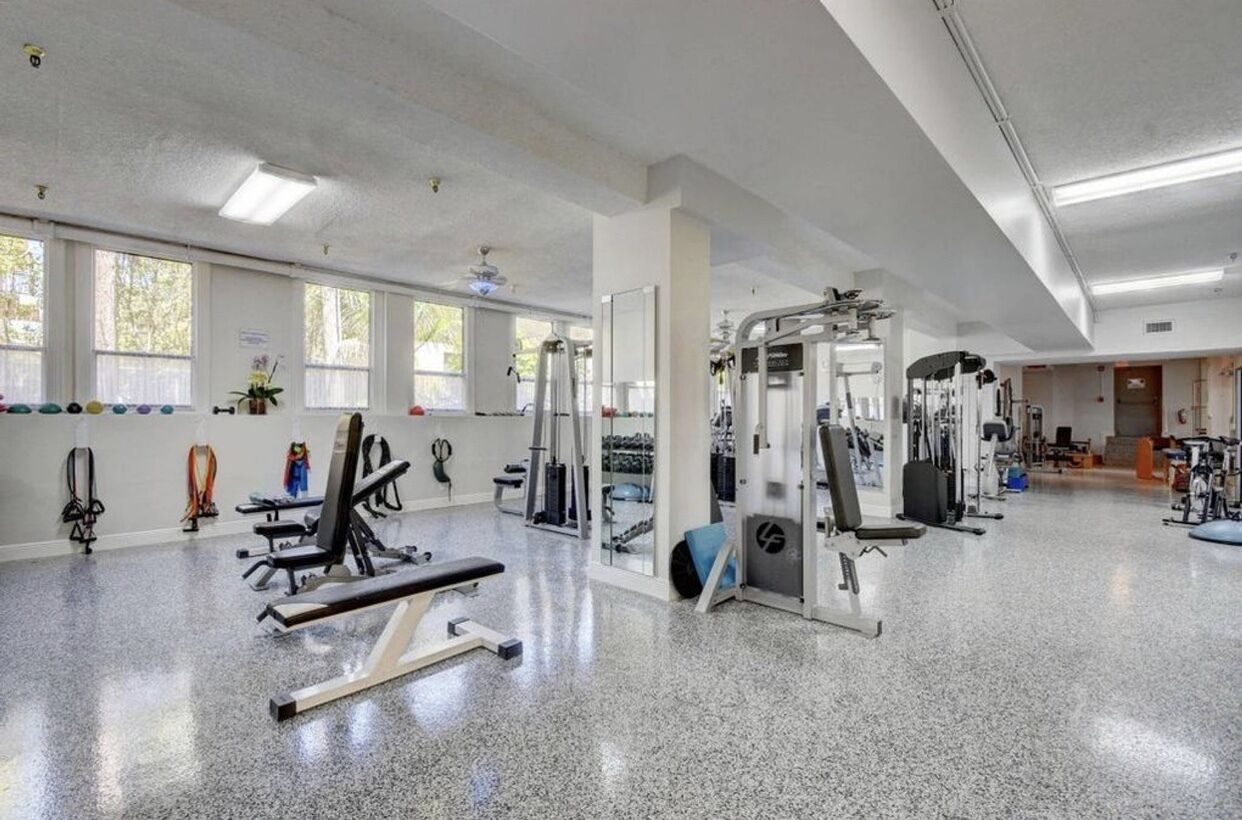 Une salle de sport spacieuse, dotée de divers équipements d’exercice, de grandes fenêtres et d’un sol propre et bien entretenu.