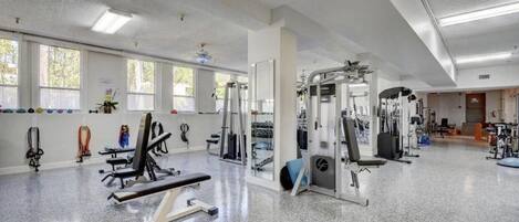 Une salle de sport spacieuse, dotée de divers équipements d’exercice, de grandes fenêtres et d’un sol propre et bien entretenu.