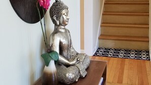 A statue of a seated figure on a wooden bench, a vase with pink flowers, and a mirror on the wall. - Serene Retreat Awaits You!  (Highland Park)