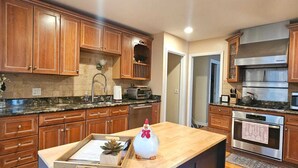 A modern kitchen with wooden cabinets, a central island, stainless steel appliances, and a blue accent wall. - Serene Retreat Awaits You!  (Highland Park)