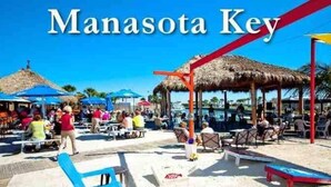 Ein Restaurant und Tiki-Bar direkt am Strand, genannt 'Manasota Key', mit Außenbereich und Sonnenschirmen.