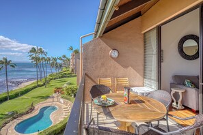 A balcony with a wooden table, chairs, and a view of the ocean.
