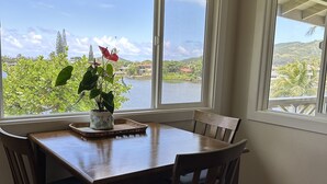 Un coin repas avec une table et des chaises en bois, de grandes fenêtres offrant une vue sur un lac et des collines.