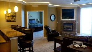 Ein Wohnzimmer mit Kamin, eine Essecke mit Bar und ein Schlafzimmer mit Bett und Kommode.