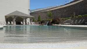 Ein Swimmingpool mit Liegestühlen, einer Laube und einem Wasserfall.