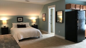 A bedroom with a bed, nightstands, a dresser, a refrigerator, and a door leading to a bathroom. - Intimate low country Carriage House with gorgeous appointments! (Bluffton)