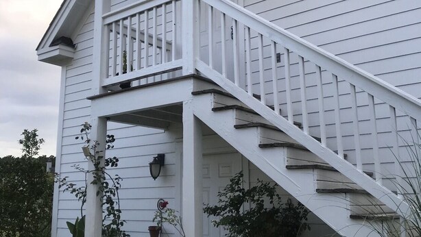 A two-story house with a white exterior, a front porch, and a staircase leading to the upper floor. - Intimate low country Carriage House with gorgeous appointments! (Bluffton)