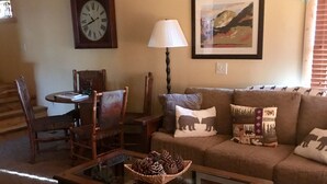 A cozy living room with a wooden coffee table, a sofa with patterned cushions, a wall clock, and a framed landscape painting. - PACK YOUR BAGS & LET THE ADVENTURES BEGIN! SLEEPS 10, HOT TUB, & PET FRIENDLY (Pagosa Springs)