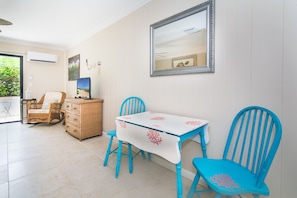 A dining area with a white table and blue chairs, a wicker chair, and a mirror on the wall. - Steps to Beach Hidden Gem Boutique Hotel (Juno Beach)