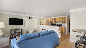 Un espace de vie compact comprenant un canapé, un téléviseur à écran plat, une kitchenette et un coin repas.