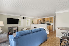 A compact living space with a sofa, a flat-screen TV, a kitchenette, and a dining area.