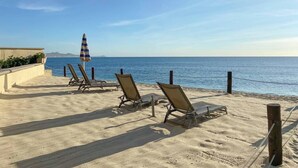 Een strand met ligbedden en een parasol, een heldere lucht en de oceaan op de achtergrond.