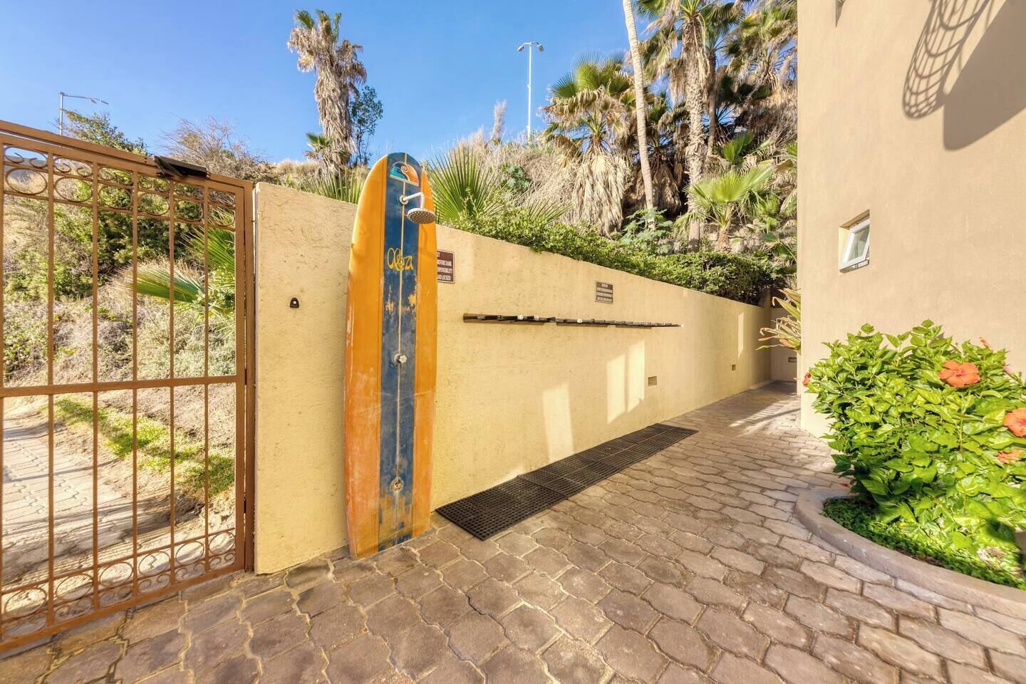 A gated entrance with a surfboard decoration, a paved pathway, and a wall with a plaque.