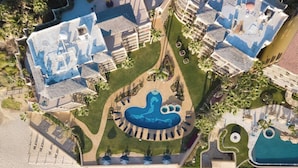 Luchtbeeld van een resort met meerdere zwembaden, een centraal rond zwembad met een dolfijnmotief en omliggende loungegedeeltes.