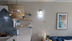 Een moderne keuken met een wit aanrecht, een hangende geweven lamp en een blauw decoratief object aan de muur.