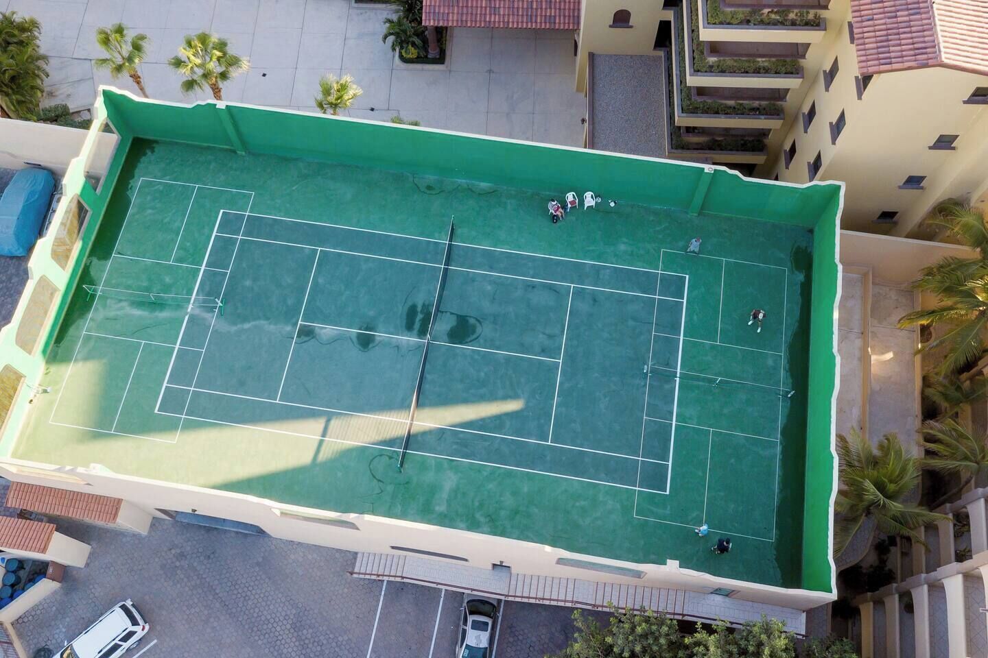 An aerial view of a tennis court with surrounding buildings and palm trees.