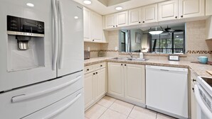 A modern kitchen with white cabinetry, a stainless steel refrigerator, a built-in water dispenser, a dishwasher, and a granite countertop. - Stunning & Serene, Minutes to Anna Maria Island, IMG & More (Bradenton)