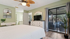 A bedroom with a large bed, a ceiling fan, a television, and a sliding glass door leading to a balcony with outdoor furniture. - Stunning & Serene, Minutes to Anna Maria Island, IMG & More (Bradenton)