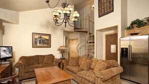 A living room with two sofas, a wooden coffee table, a TV, and a chandelier. There is a staircase leading to an upper level. - Amazing Mountain Condo with a Loft (Keystone)
