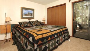 A bedroom with a bed, two bedside lamps, a framed picture on the wall, a wooden door, and a sliding glass door leading to an outdoor area. - Amazing Mountain Condo with a Loft (Keystone)