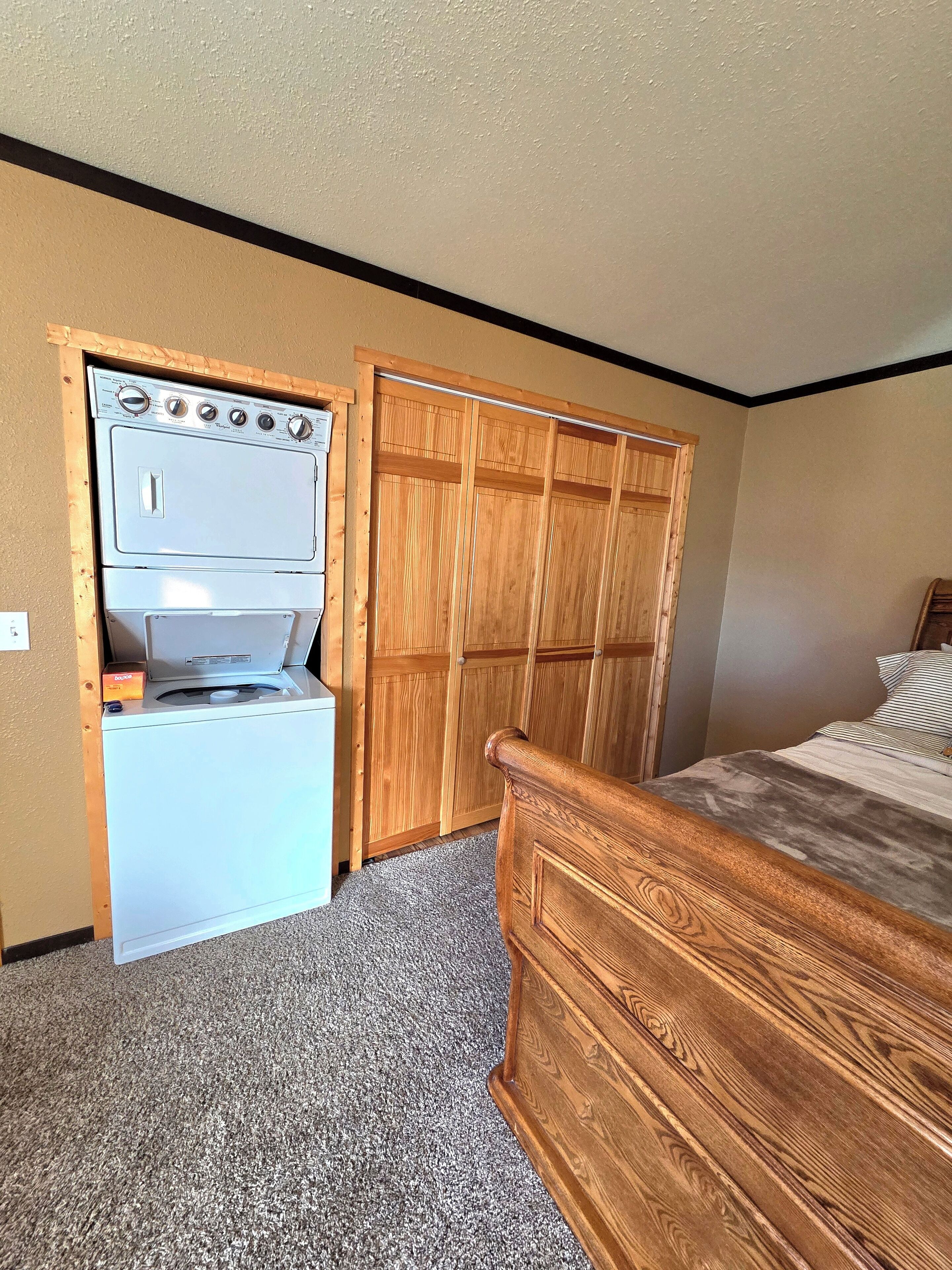 A bedroom with a wooden bed, a white washing machine, and a wooden wardrobe.