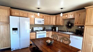 A kitchen with wooden cabinets, a white refrigerator, a microwave, a stove, and a dining table with chairs. - Lake Front Rental With Chugach Mountain Views! (Glennallen)