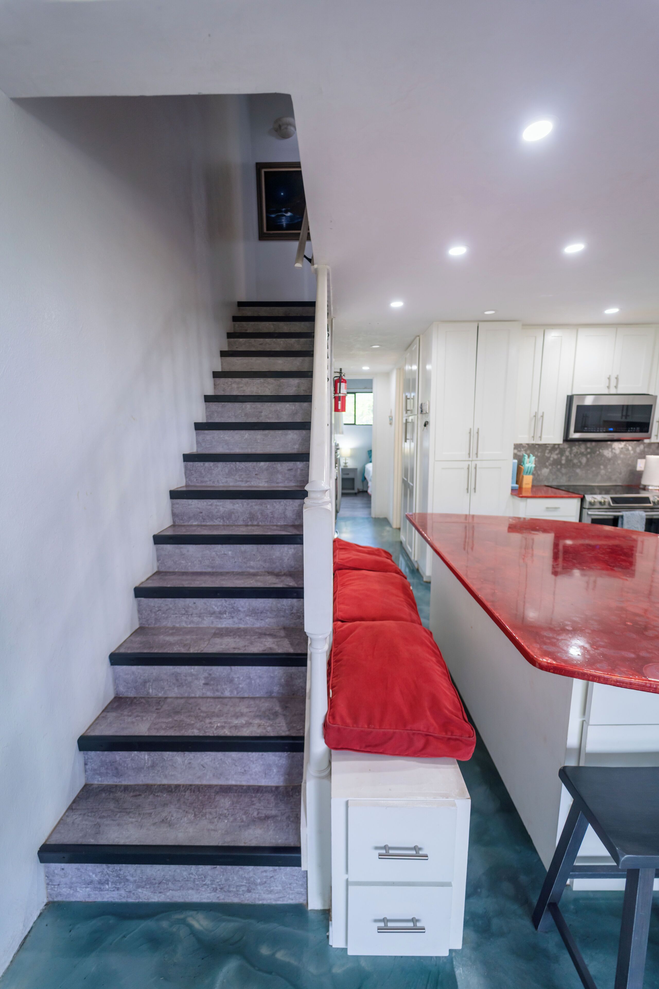 Un escalier menant à une cuisine avec des meubles blancs et un plan de travail rouge.