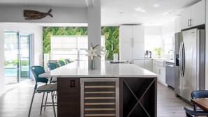 A modern kitchen with a central island, stainless steel appliances, and a view of greenery through large windows. - ☆Featured on HGTV☆ Heated Pool, SleepNumber Beds, Beach Cruisers (Largo)