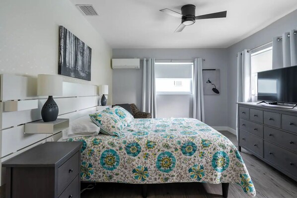 A bedroom with a bed, bedside tables, a dresser, a ceiling fan, and a TV.