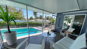A modern outdoor seating area with a pool view, white lounge chairs, and a small table with a plant. - ☆Featured on HGTV☆ Heated Pool, SleepNumber Beds, Beach Cruisers (Largo)