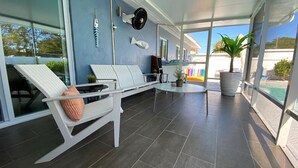 A covered outdoor seating area with white chairs and a table, large windows, and a potted plant. - ☆Featured on HGTV☆ Heated Pool, SleepNumber Beds, Beach Cruisers (Largo)