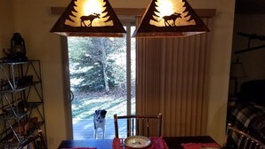 A dining area with a table set for four, two pendant lights with animal silhouettes, a view of a dog outside, and a window with curtains. - Enjoy Our Mountain Retreat in The Teton Valley adjacent to Jackson Hole (Victor)