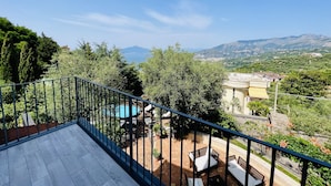 Un balcón con vista a una piscina, mobiliario de patio y un paisaje montañoso.